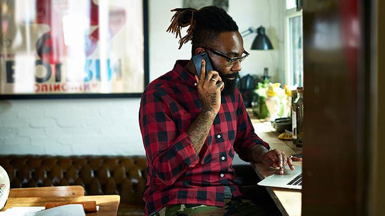 Adult man working on his laptop while also on the phone.